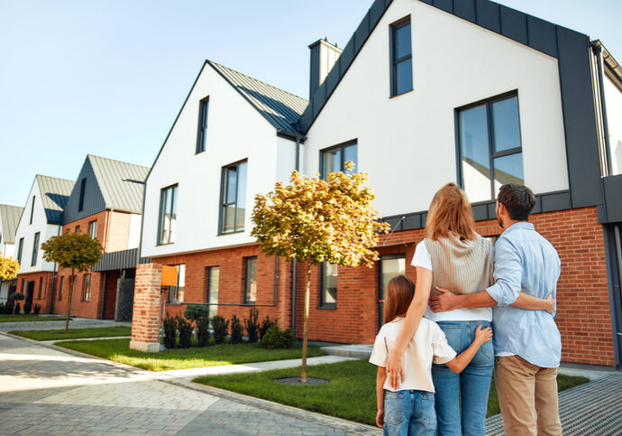 A young happy family with a child hugging each other are standing and looking on the street at their new home. Renting and buying real estate. Moving concept.