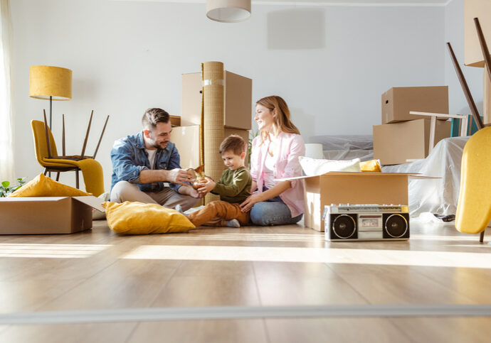 Happy family with one child starting new life in new apartment. They are unpacking boxes and talking to the child while sitting on the floor